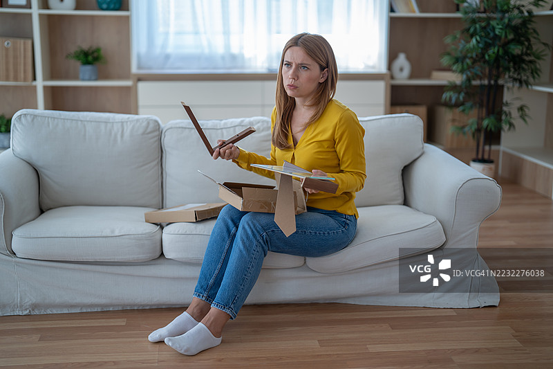 女人坐在沙发上检查从网上商店送来的破损相框图片素材