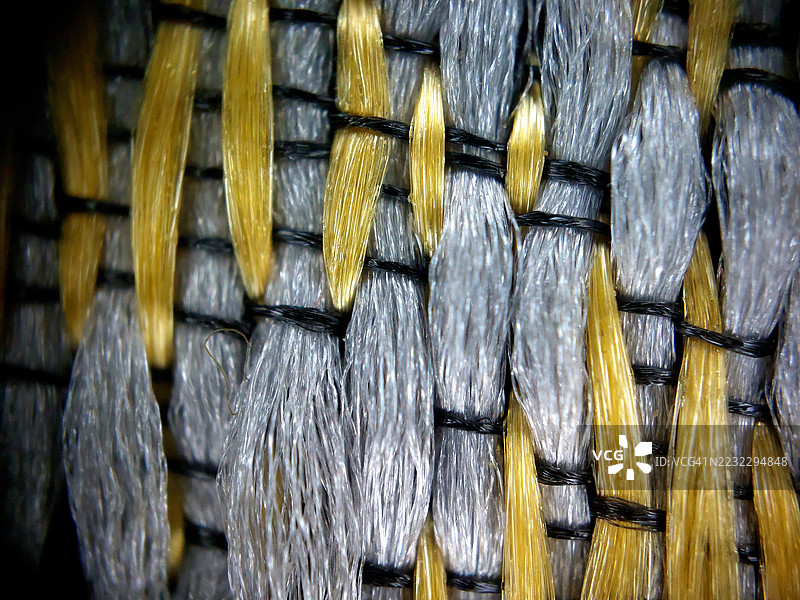 极端微距特写，展示交织的金色和灰色合成纤维线的编织织物，细节丰富。图片素材