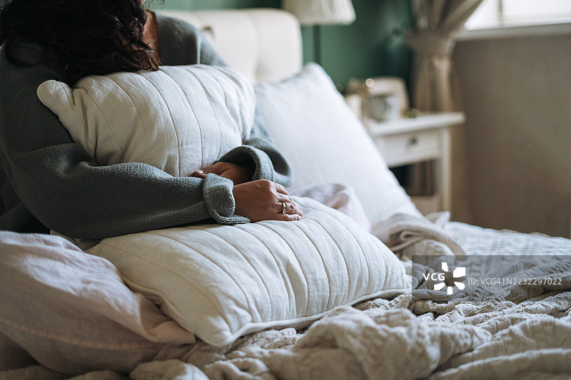 年轻女性在家中床上休息，怀抱枕头，享受舒适的早晨。图片素材