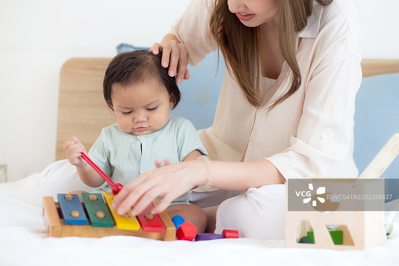 亚洲母亲在家中的卧室里与女儿快乐地玩耍，妈妈用玩具陪伴女儿，促进她的成长与发展，家庭生活，学习教育，家庭与生活方式。图片素材