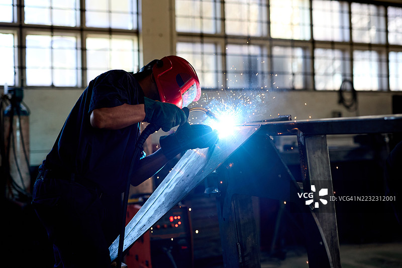 工人在工业车间焊接钢材，四周飞溅着火花，穿着防护装备图片素材