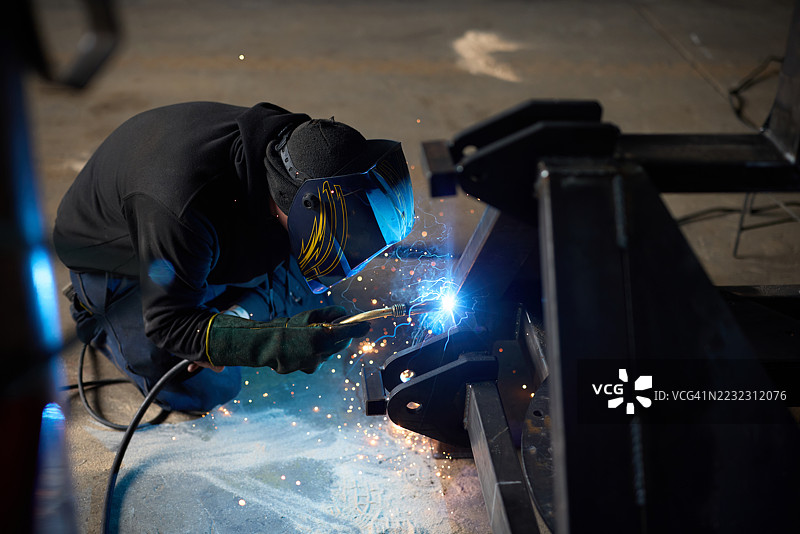 工人在工业厂房中认真焊接钢铁，四周飞溅着明亮的火花图片素材
