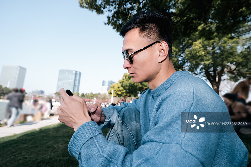 年轻的亚洲男子在城市户外看手机图片素材