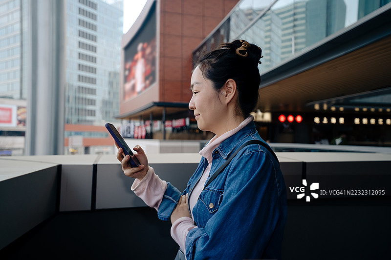 年轻的东亚女性在城市户外看手机图片素材