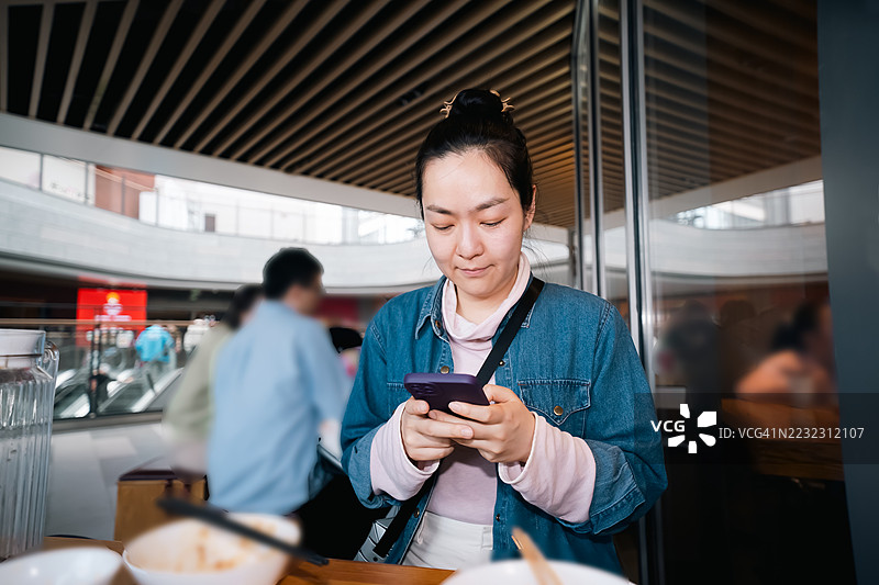 年轻的东亚女性在一家休闲餐厅里看手机图片素材