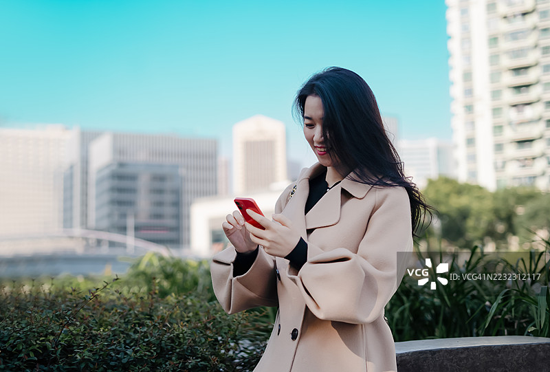 年轻的东亚女性在城市户外看手机图片素材