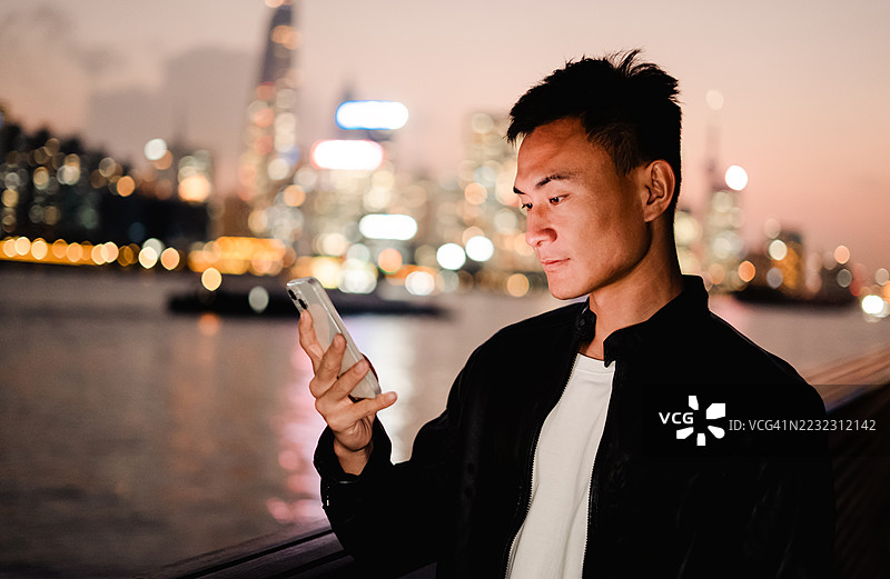 年轻的亚洲男子在城市户外看手机图片素材