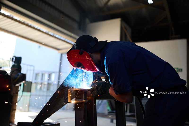 工人在工业车间焊接钢材，四周飞溅着火花，穿着防护装备图片素材