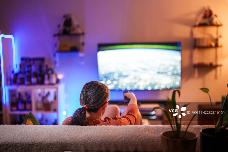 女人在舒适的客厅里用遥控器看电视图片素材