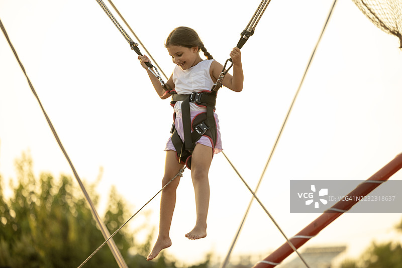小女孩在蹦床上快乐地做着四周翻腾，兴奋地笑着。图片素材