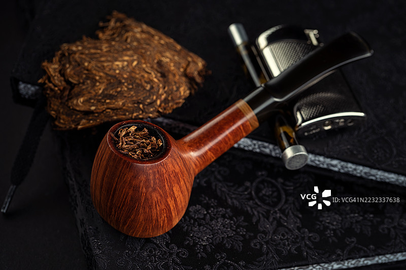 直纹高端奥地利设计的火山形烟斗放在一本书上，旁边有一个打火机和一个烟斗工具。图片素材