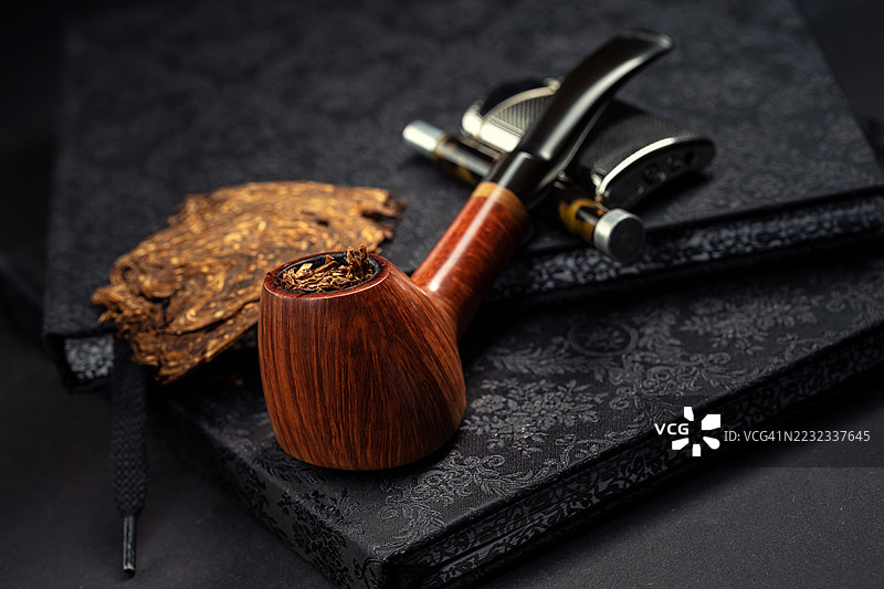 直纹高端奥地利设计的火山形烟斗放在一本书上，旁边有一个打火机和一个烟斗工具。图片素材