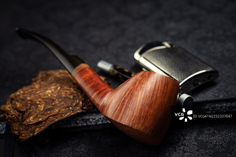 直纹高端奥地利设计的火山形烟斗放在一本书上，旁边有一个打火机和一个烟斗工具。图片素材