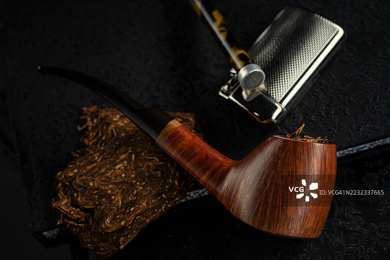 直纹高端奥地利设计的火山形烟斗放在一本书上，旁边有一个打火机和一个烟斗工具。图片素材