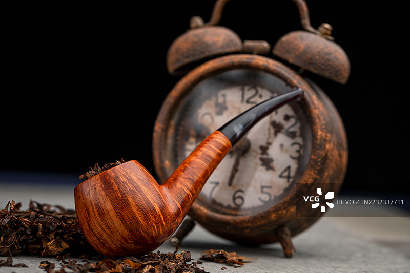 高端意大利设计的直纹烟斗，鹰嘴形状，放在闹钟前。图片素材