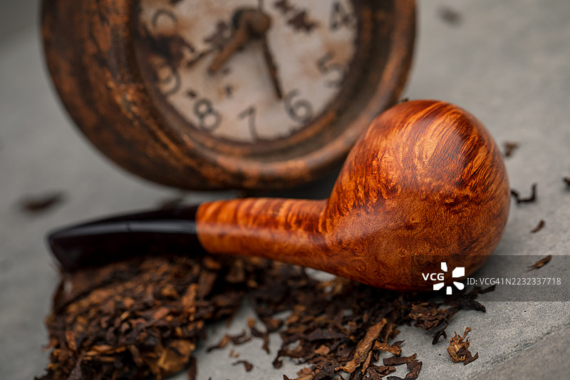 高档意大利设计的直纹烟斗，鹰嘴形状，放在闹钟前。图片素材