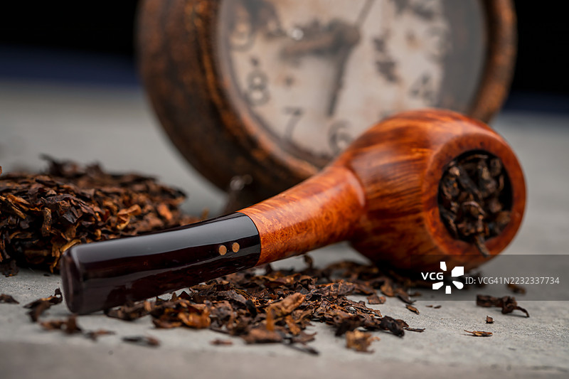 高端意大利设计的直纹烟斗，鹰嘴形状，放在闹钟前。图片素材