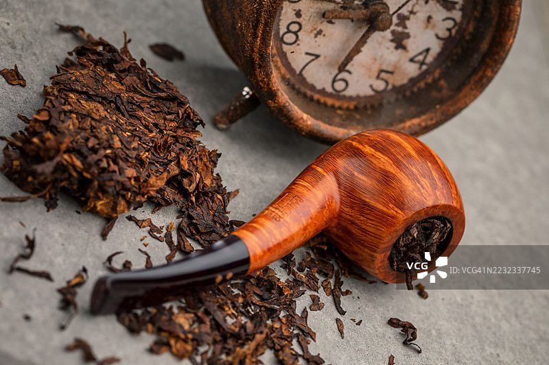 高档意大利设计的直纹烟斗，鹰嘴形状，放在闹钟前。图片素材