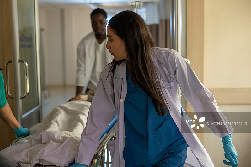 医务人员在明亮的医院灯光下紧急将一名患者用担架送入急救室，医生和护士们穿着防护手套在紧急协助。图片素材