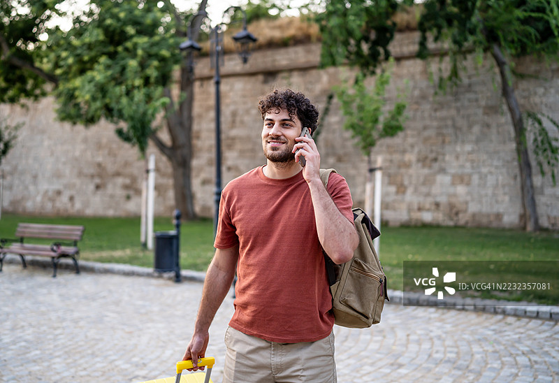 年轻男性游客一边走一边打电话，拖着行李。图片素材