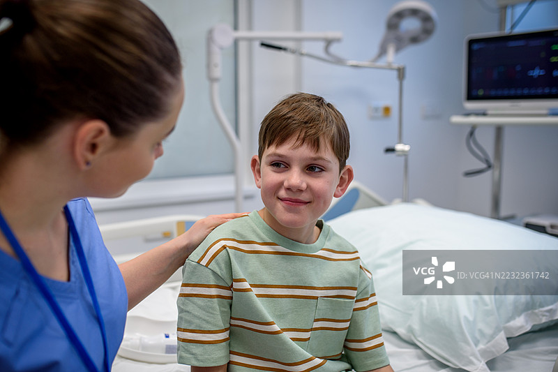 关心的护士在急诊室与年轻男孩病人交谈。图片素材