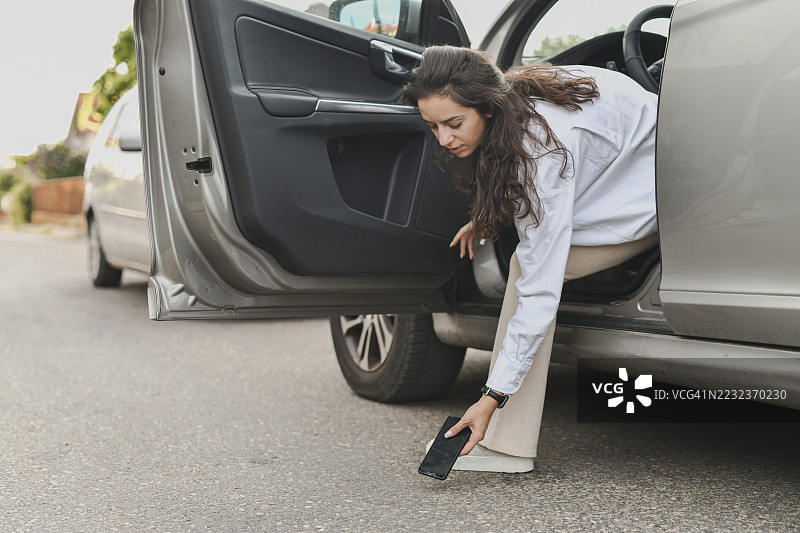 女子在车旁，因手机掉落而担忧地拿着碎屏手机图片素材