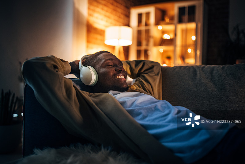 年轻黑人男子在家中放松，夜晚聆听音乐图片素材