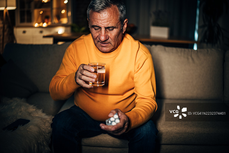 老年人在安静的夜晚时光中，手握一杯水和药物，静静地思考。图片素材