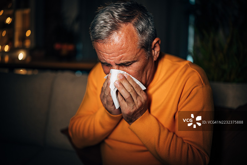 夜晚，老年男子独自在家中坐着，手握纸巾，面对情感。图片素材