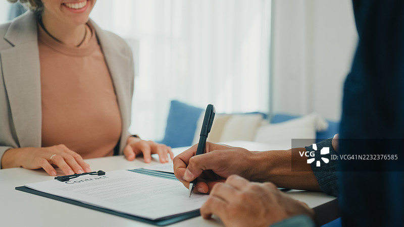 年轻夫妇在家客厅与财务顾问签署财务协议的特写镜头。财务规划与生活方式概念。图片素材