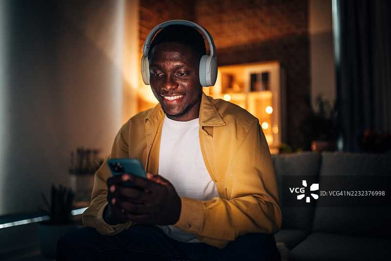 年轻黑人男性在家中夜晚享受音乐并使用智能手机图片素材
