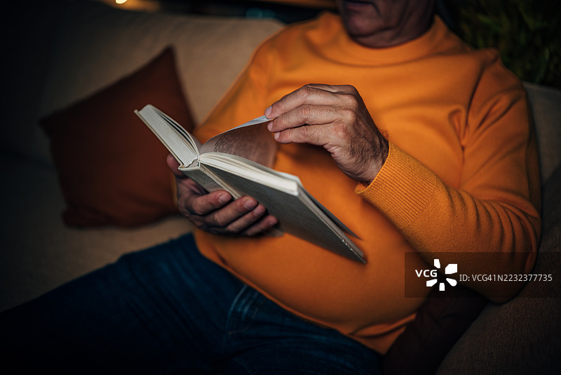 老年人在舒适的室内环境中享受安静的夜晚，阅读一本书。图片素材