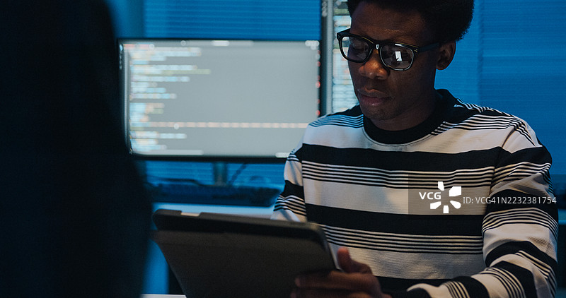 一群IT专业人士在夜间办公室内使用平板电脑和笔记本电脑合作进行网络安全和数据分析。软件开发者、人工智能和编程。图片素材