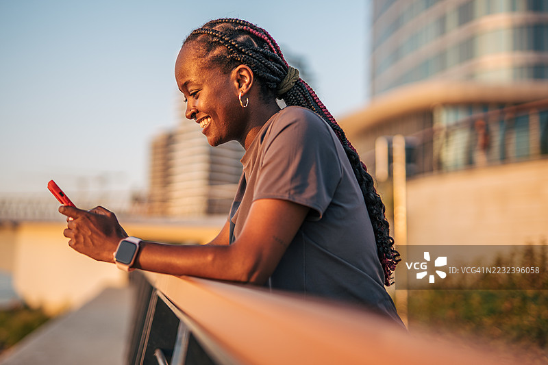 微笑的女运动员在训练后使用智能手机图片素材