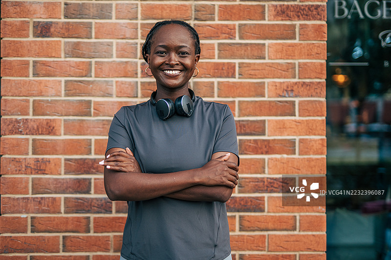 自信的运动员微笑着，双臂交叉靠在砖墙上图片素材