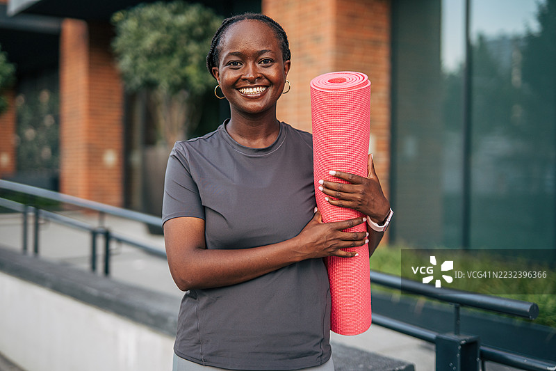 微笑的黑人女性在户外训练后手持瑜伽垫图片素材