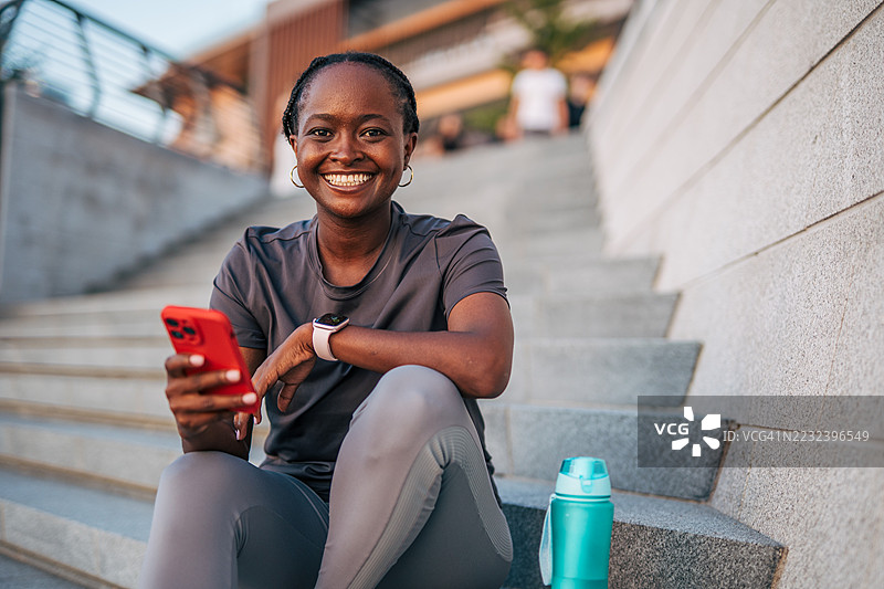 微笑的女运动员坐在城市台阶上使用智能手机图片素材