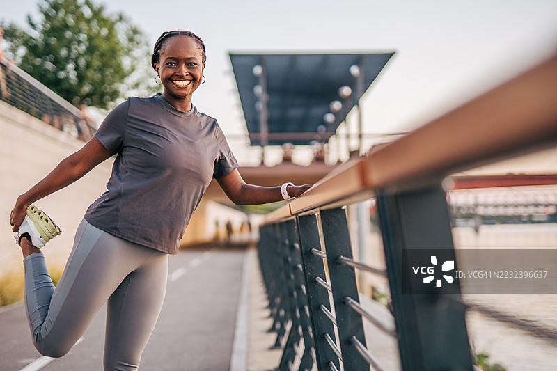 微笑的女运动员在城市河边拉伸腿部图片素材