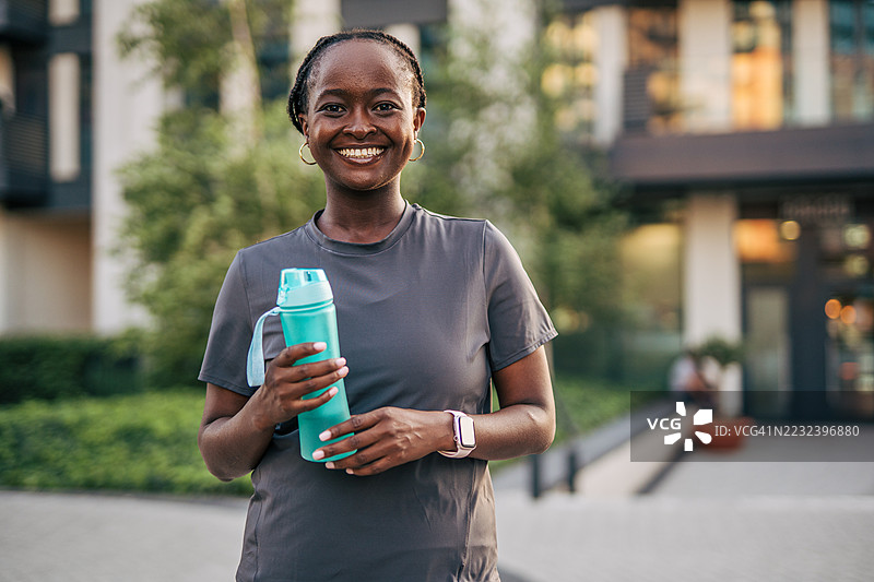 微笑的黑人女性在户外锻炼后手持水瓶图片素材