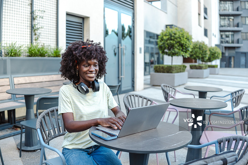 在现代咖啡馆环境中，戴着耳机的女性在户外使用笔记本电脑图片素材