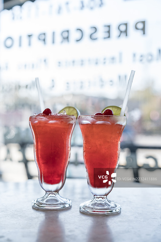 两杯玻璃饮料，上面放着樱桃，摆放在老式药店的石材桌子上。图片素材