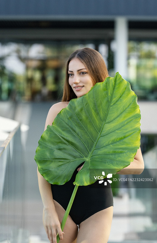 户外手持大型热带叶子的女性图片素材