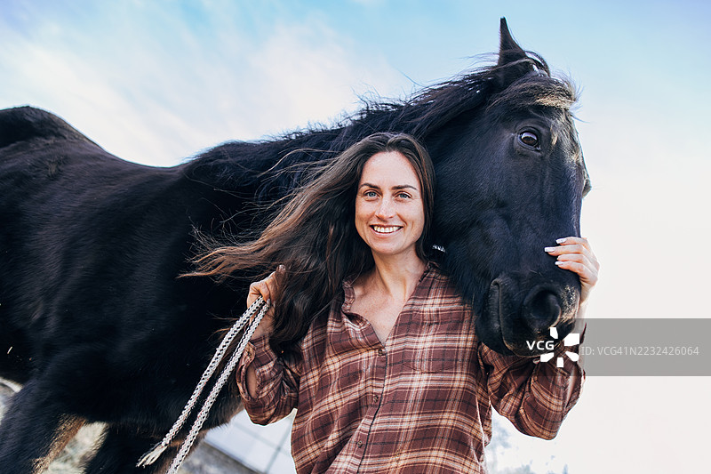 女人在阳光明媚的日子里温柔地拥抱她的黑马图片素材