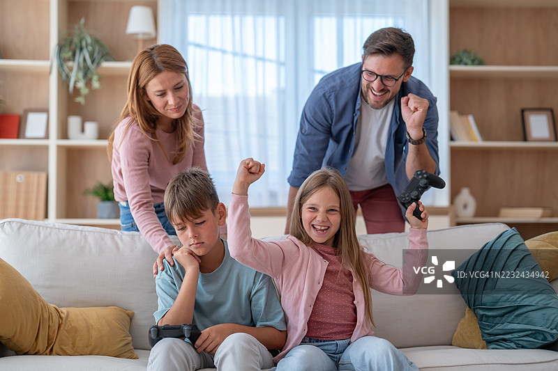 家庭在家玩电子游戏：女儿获胜，儿子失利图片素材