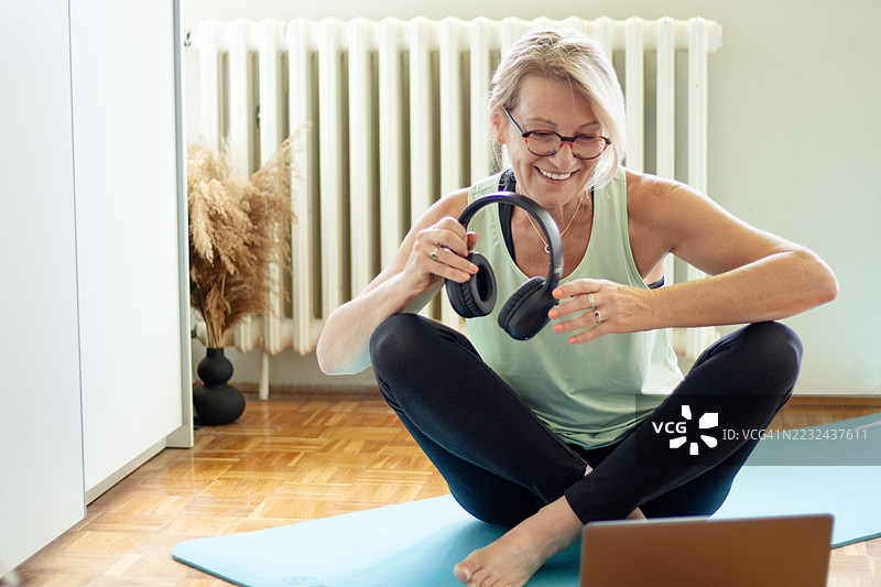 成熟的金发女性在公寓的瑜伽垫上使用笔记本电脑进行在线锻炼图片素材