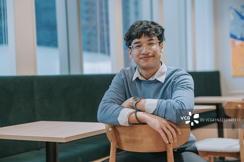 年轻的亚洲男子自信地微笑，坐在现代咖啡馆里图片素材