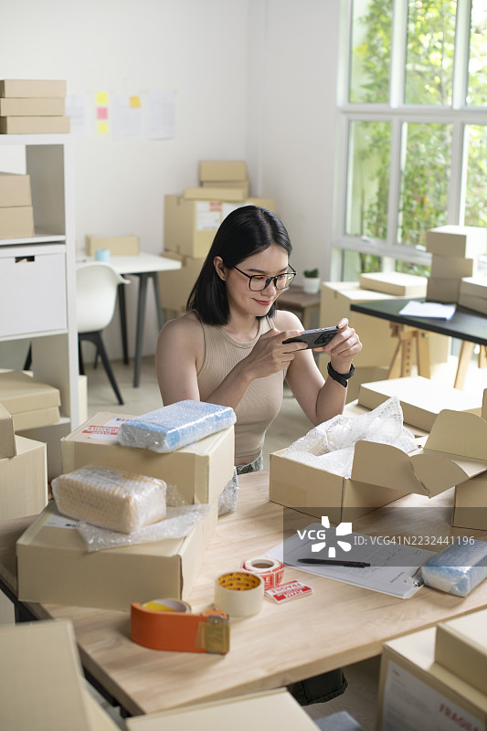 女性在线商店小企业主卖家企业家在桌子上打包邮寄包裹，准备发货。电子商务代发货服务概念。图片素材