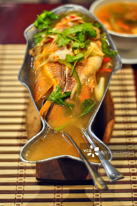一整条蒸鱼在清汤中盛放于不锈钢鱼形盘上，特写镜头。图片素材
