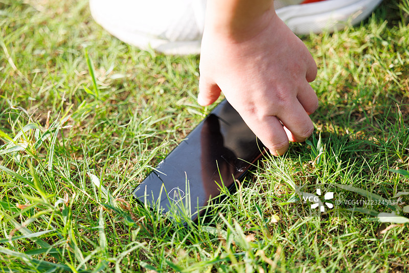 手机屏幕保护膜掉到地上碎了，一只手拿着手机检查损坏情况。图片素材