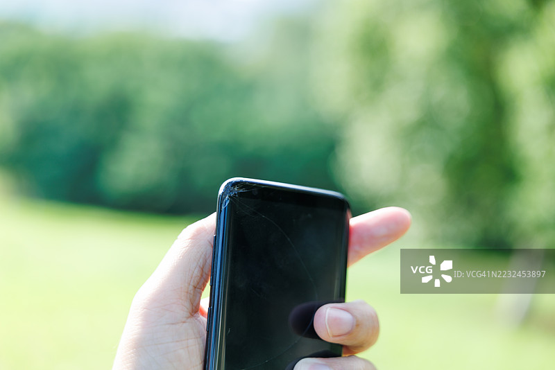 手机屏幕保护膜掉落在地上碎裂了，一只手拿着手机检查损坏情况。图片素材